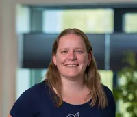 Portret van een vrouw van begin veertig met schouderlang blondbruin haar, gekleed in een donkerblauw T-shirt met bloemenprint en jeans, glimlachend op het Twyzer kantoor.