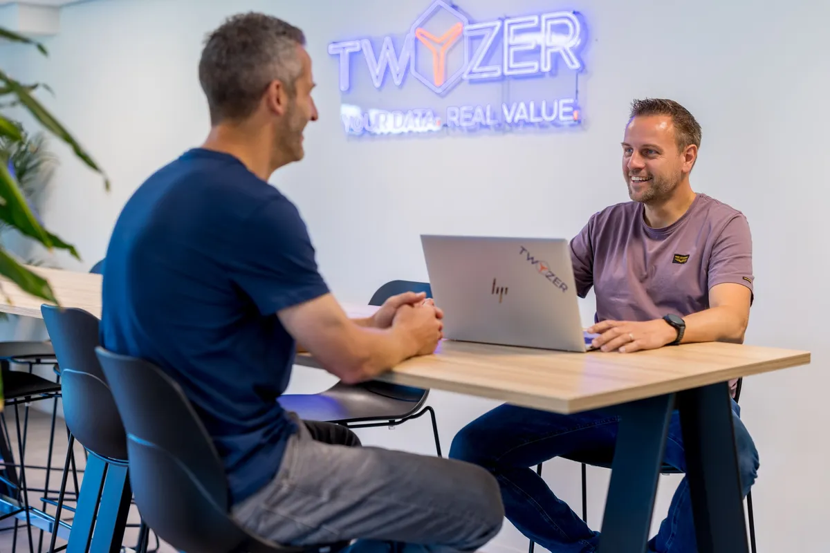 Perry Lambrechts en een collega in gesprek aan een tafel in het Twyzer-kantoor met neon bedrijfslogo